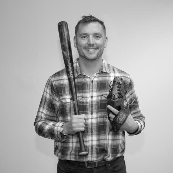 A smiling man wearing a baseball glove and holding a bat